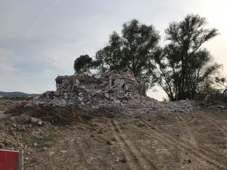 Góra gruzu i cegieł pozostała po rozbiórce budynku, z widocznymi fragmentami konstrukcji i drzewami w tle.