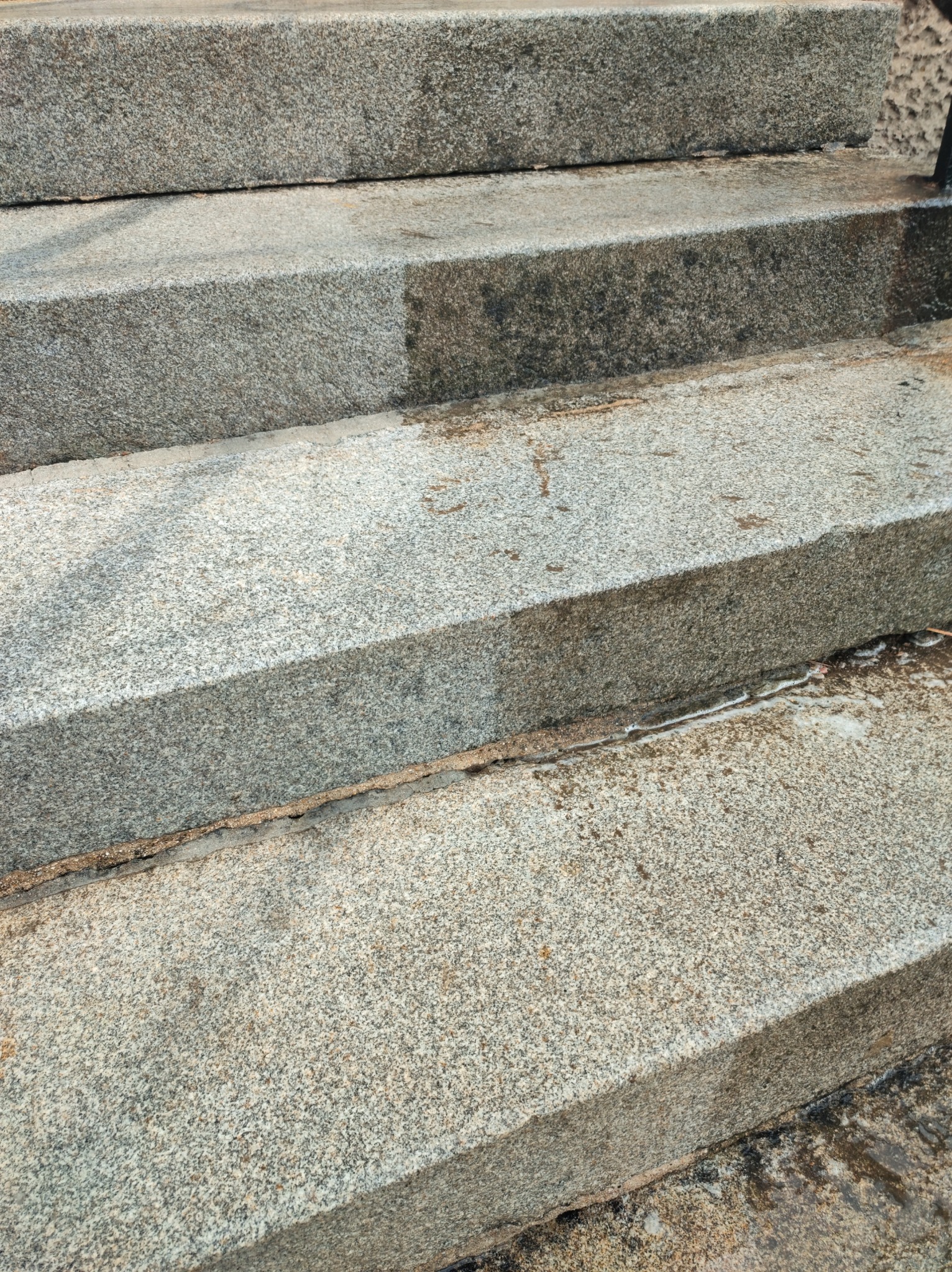 Kamienne schody, częściowo umyte, z widocznym kontrastem między czystą a brudną powierzchnią, z resztkami wody w szczelinach.