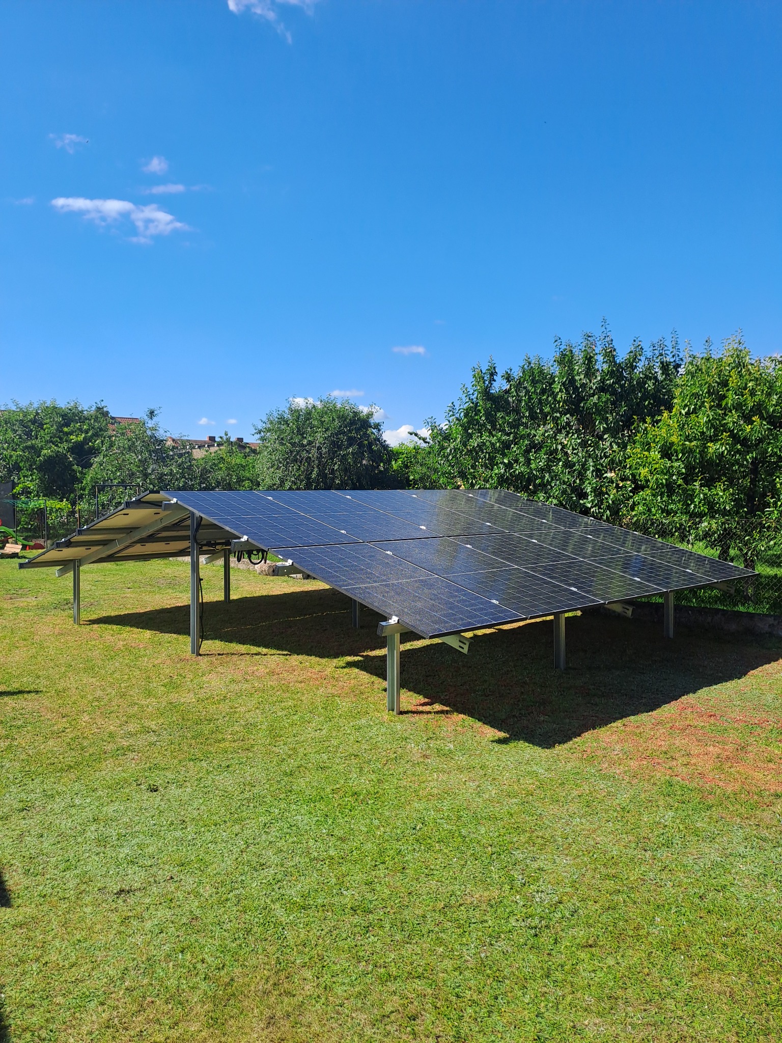 Instalacja paneli słonecznych na metalowej konstrukcji, umieszczona na trawniku w ogrodzie, widok w słoneczny dzień.