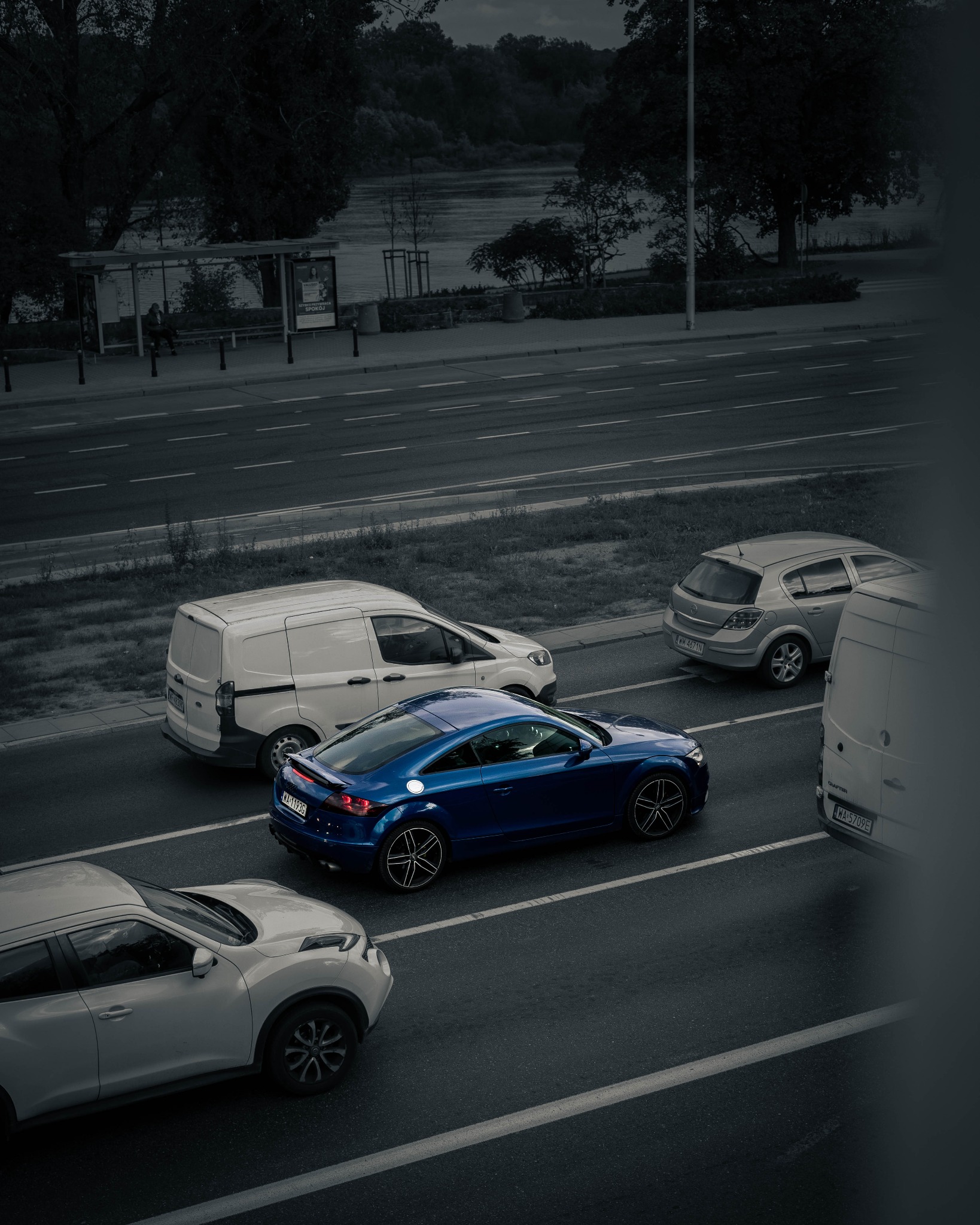 Niebieskie sportowe coupe na drodze miejskiej, otoczone innymi pojazdami, widok z góry.