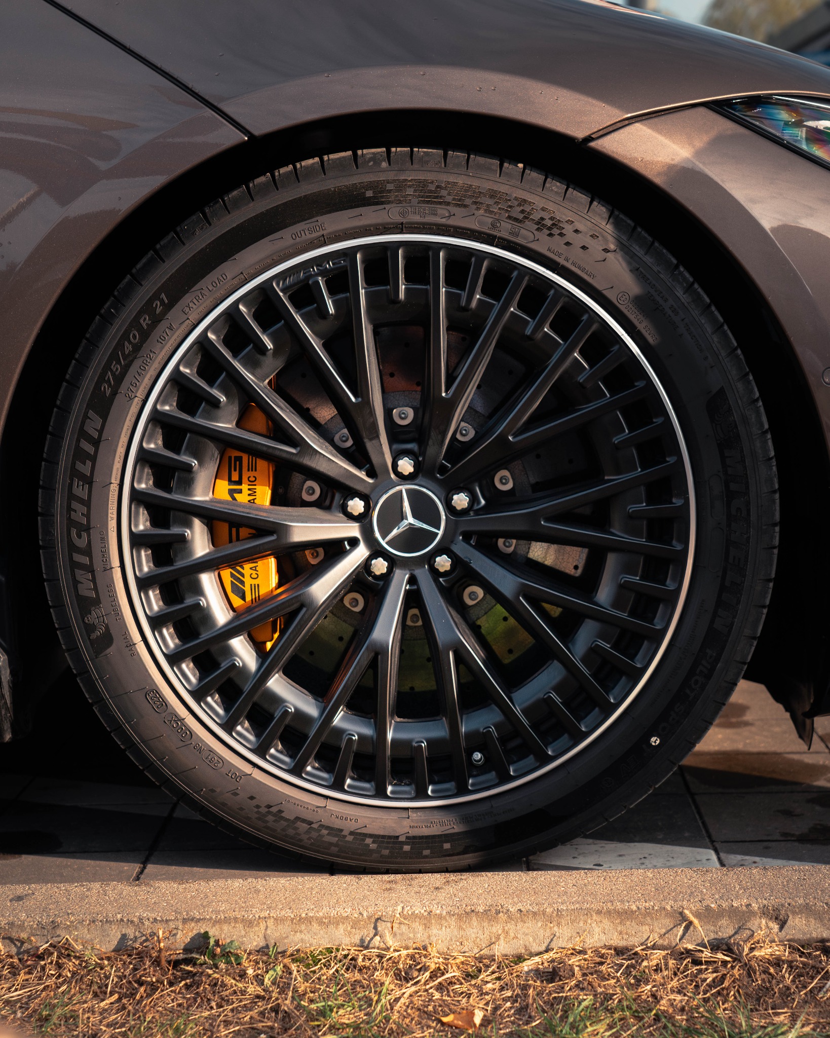 Czarno-srebrna felga aluminiowa z oponą Michelin na brązowym samochodzie Mercedes AMG, z żółtymi zaciskami hamulcowymi AMG.