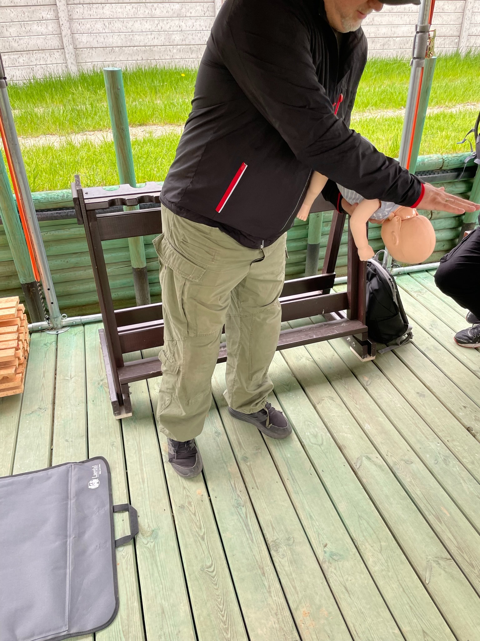 Instruktor demonstruje manewr Heimlicha na fantomie niemowlęcia podczas kursu pierwszej pomocy, w tle widoczna torba Laerdal.