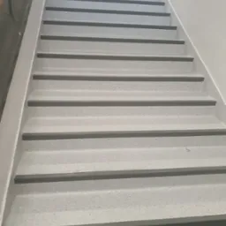 Schody pokryte szarą wykładziną z antypoślizgowymi listwami na krawędziach stopni, widok z dołu.