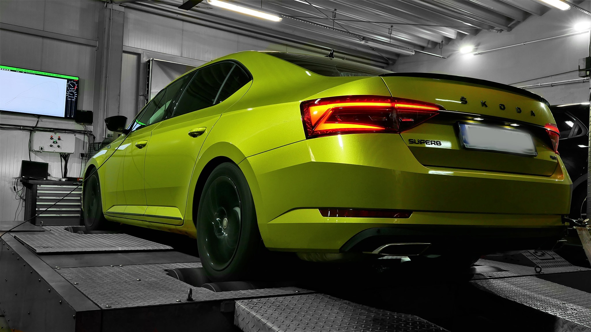 Żółta Skoda Superb na hamowni podwoziowej podczas testów, widoczny monitor z wynikami pomiarów.