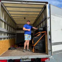 Pracownik transportowy zabezpiecza mebel folią i pasami wewnątrz busa. Widoczne tablice rejestracyjne PL i napis CRAFTER.