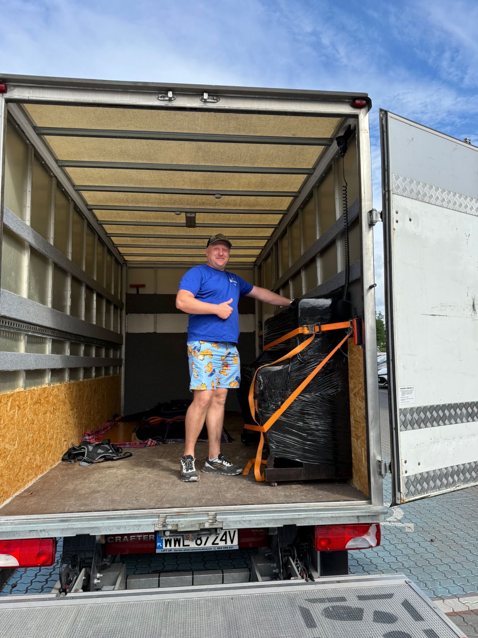 Pracownik transportowy zabezpiecza mebel folią i pasami wewnątrz busa. Widoczne tablice rejestracyjne PL i napis CRAFTER.