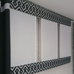 Firma Ewa - Roleta rzymska z geometrycznym wzorem w kolorze czarnym i srebrnym, widoczna z dołu, z dekoracyjnymi czarnymi zasłonami po lewej stronie.