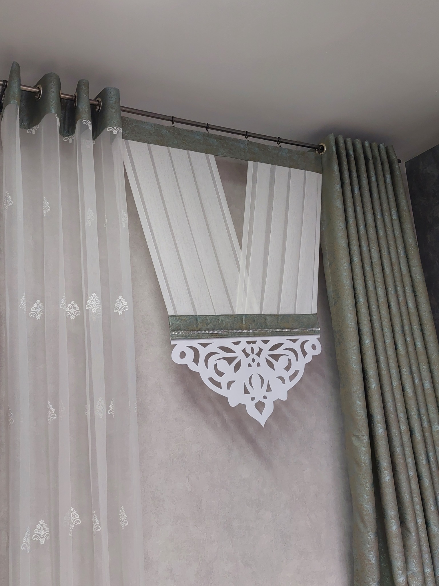 Delikatne, białe zasłony z subtelnym wzorem i dekoracyjnym, ażurowym elementem w Częstochowie, zawieszone na karniszu z zielonymi akcentami.
