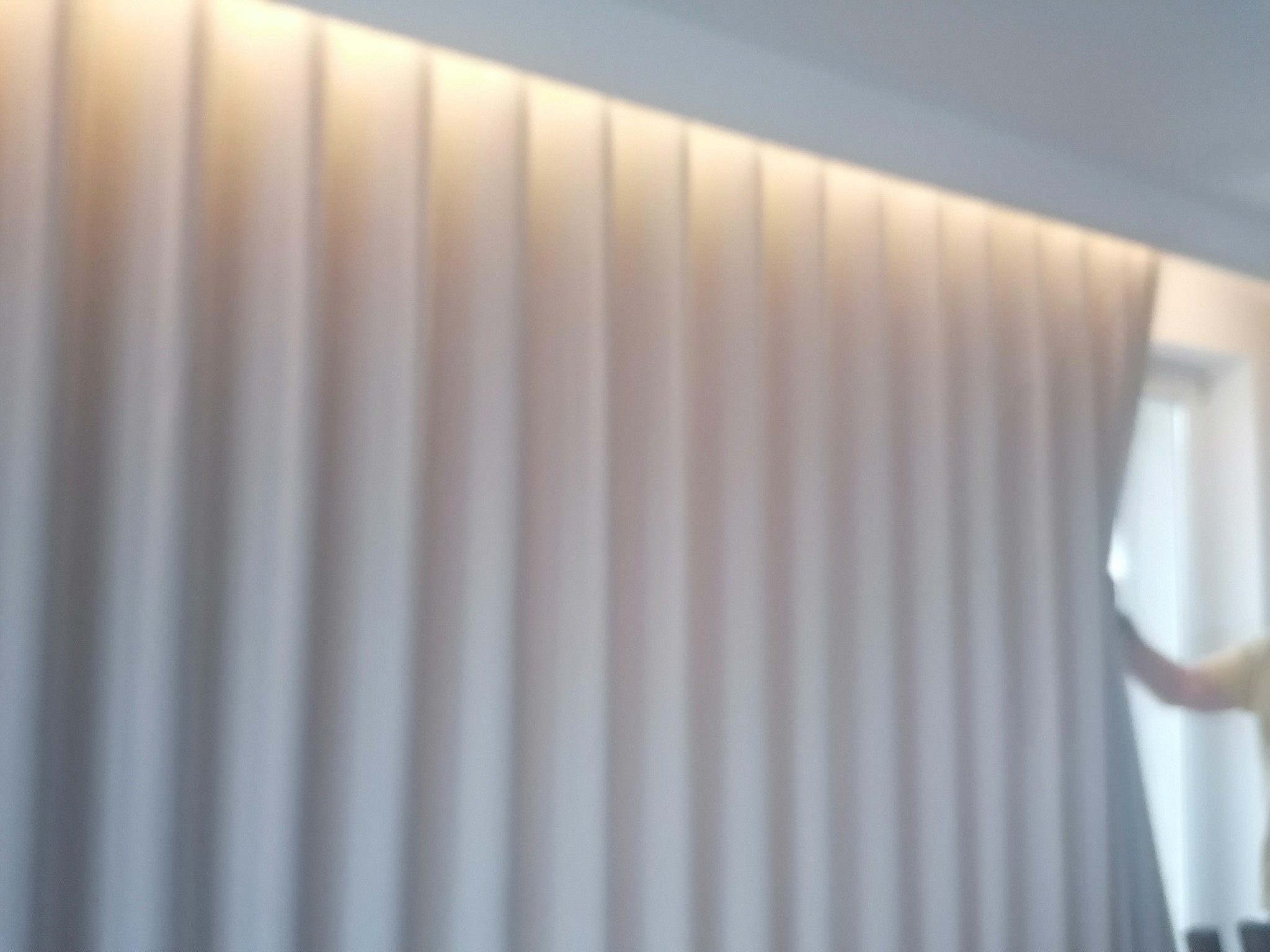 Delikatne, jasne zasłony z subtelnym oświetleniem górnym w tle okno i fragment sylwetki osoby.