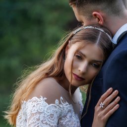 KOMP-BOX Urszula Gajewska - Romantyczne ujęcie panny młodej w koronkowej sukni, opierającej głowę o ramię pana młodego. Delikatna biżuteria i stonowany makijaż podkreślają subtelność chwili.