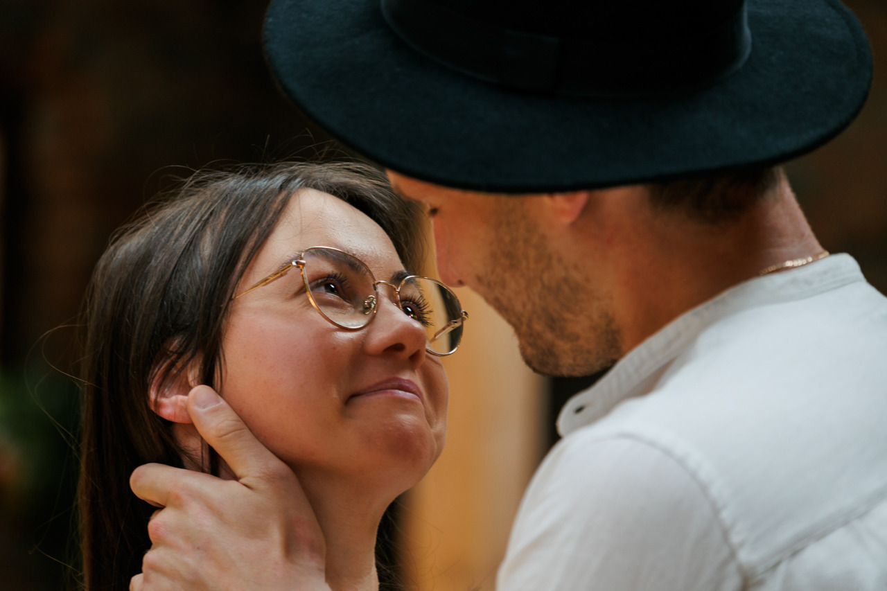 Zakochana para z Wejherowa: ona w okularach, on w kapeluszu, patrzą sobie w oczy. Delikatne światło podkreśla intymną chwilę.