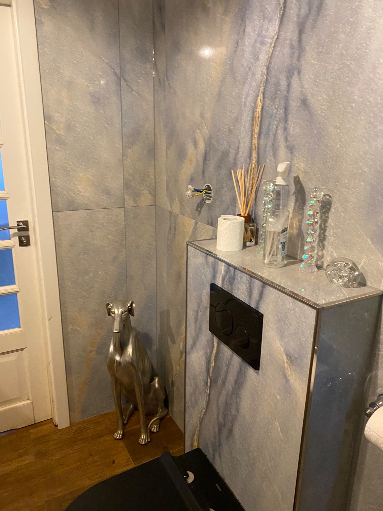 Wykończona łazienka w Lublinie z płytkami imitującymi marmur, srebrną figurką psa rasy chart i elementami dekoracyjnymi na zabudowie WC.