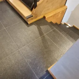 Granitowa posadzka z widocznymi schodami drewnianymi z czarną balustradą i oświetleniem punktowym w ścianie.