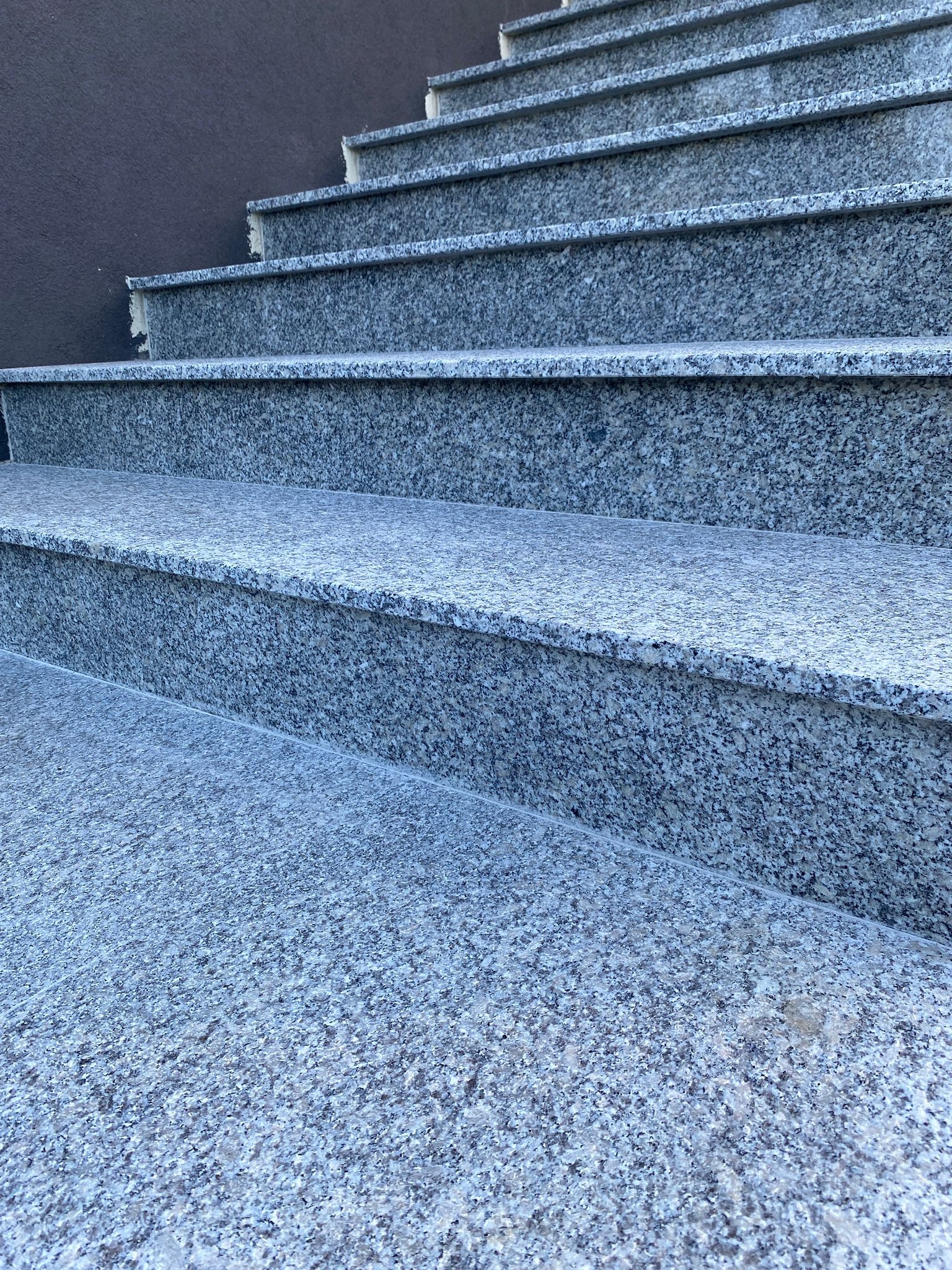 Zewnętrzne schody z szarego kamienia z widoczną strukturą granitu, prowadzące w górę wzdłuż ciemnej ściany.