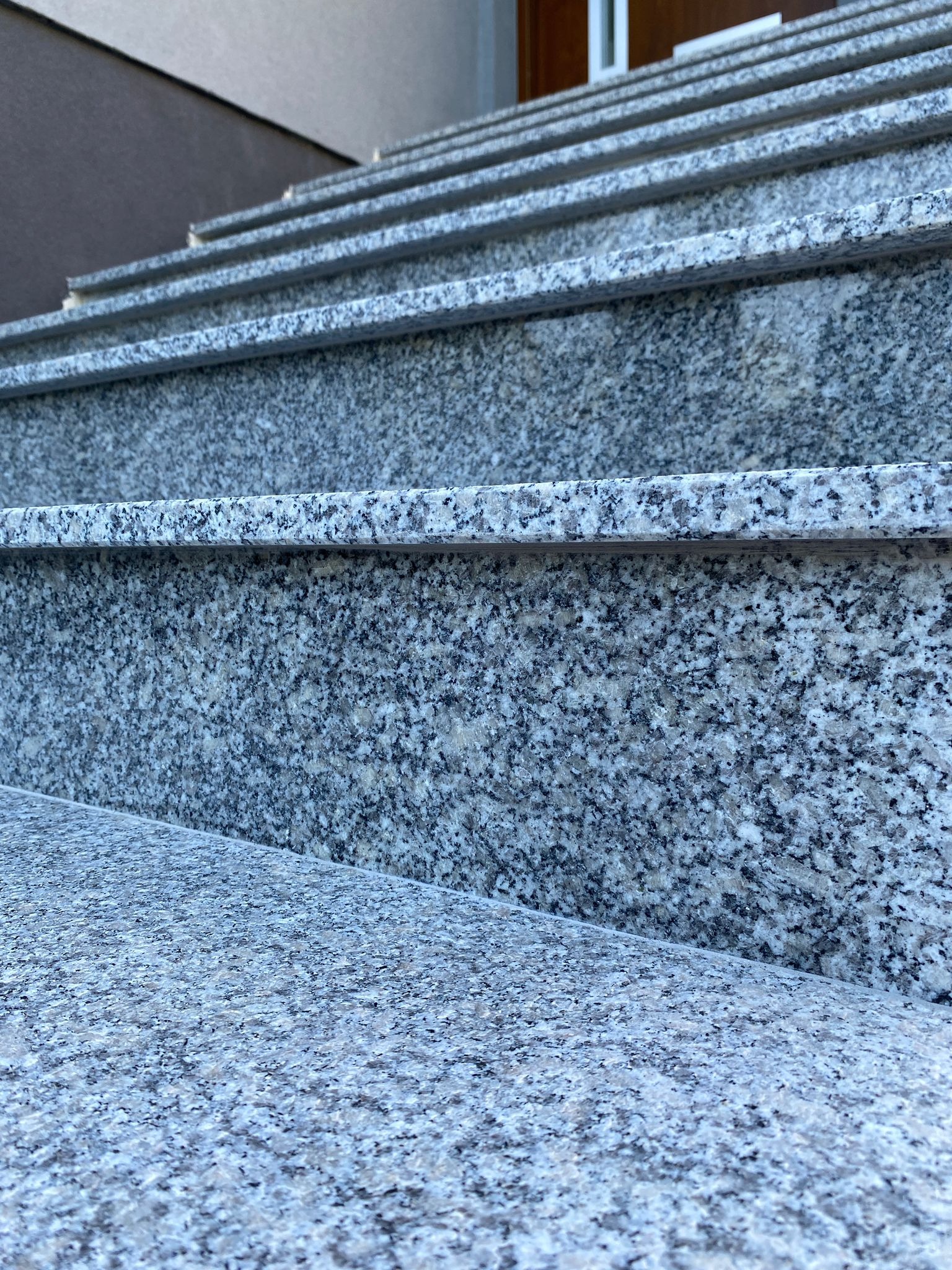 Szare, granitowe schody zewnętrzne z widoczną fakturą kamienia, prowadzące do drzwi wejściowych.