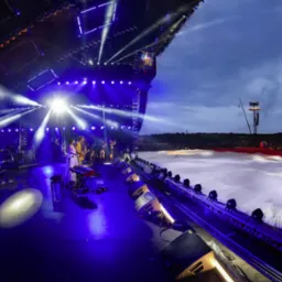 Zespół Kwiat Jabłoni na scenie podczas koncertu Pol'and'Rock, oświetlony niebieskimi światłami, z widoczną biało-czerwoną flagą w tle i tłumem publiczności.