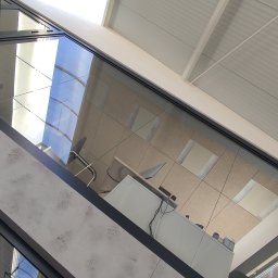 Clinox - Profesjonalne pranie kanap i tapicerki meblowej Warszawa - Wnętrze biura z widokiem na sufit z oknami dachowymi, biurko z komputerem i krzesłem, widziane z perspektywy nisko położonej ściany z elementami szklanymi.