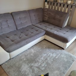 Clinox - Profesjonalne pranie kanap i tapicerki meblowej Warszawa - Szara narożna kanapa z jasną bazą i szary dywan w trakcie czyszczenia parowego; widoczna dysza i zbiornik odkurzacza piorącego.