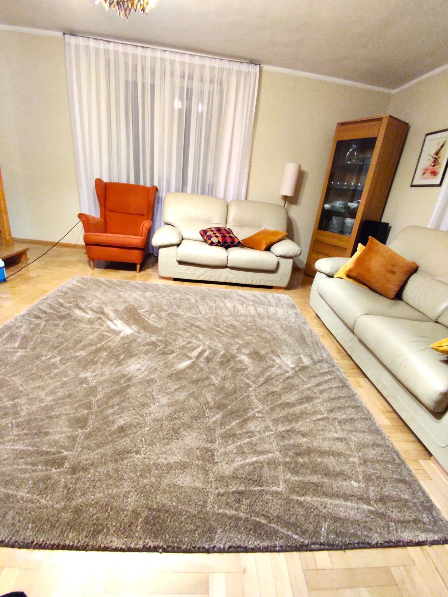 Beżowy dywan shaggy z geometrycznym wzorem w salonie z kremowymi sofami i pomarańczowym fotelem uszakiem