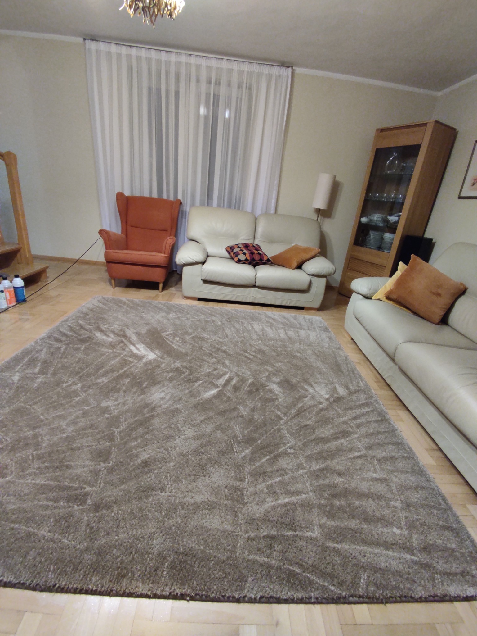 Beżowy dywan shaggy z geometrycznym wzorem w salonie z kremowymi kanapami i pomarańczowym fotelem uszakiem.