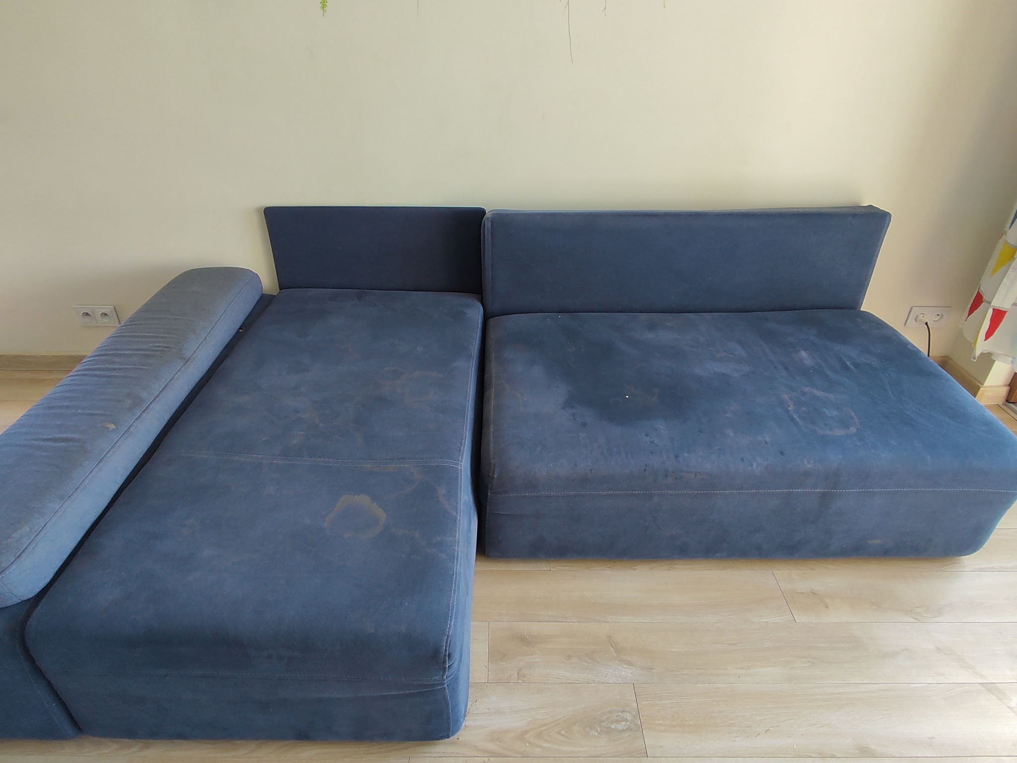 Niebieska, modułowa kanapa z wyraźnymi plamami na tapicerce, stojąca na podłodze z paneli.