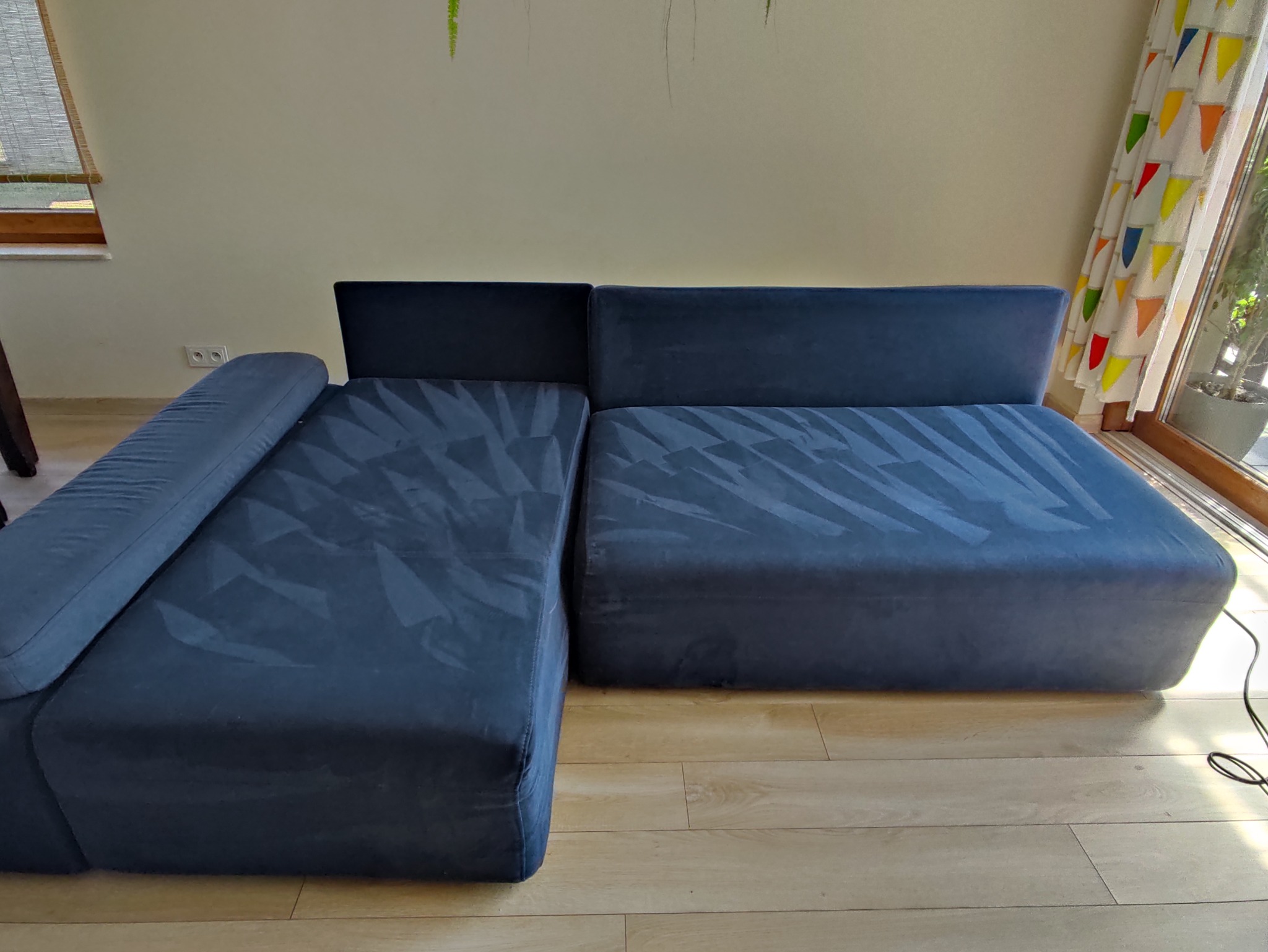 Narożnik modułowy w odcieniach granatu z widocznymi śladami po czyszczeniu tapicerki, ustawiony na jasnej podłodze w pokoju z oknem.