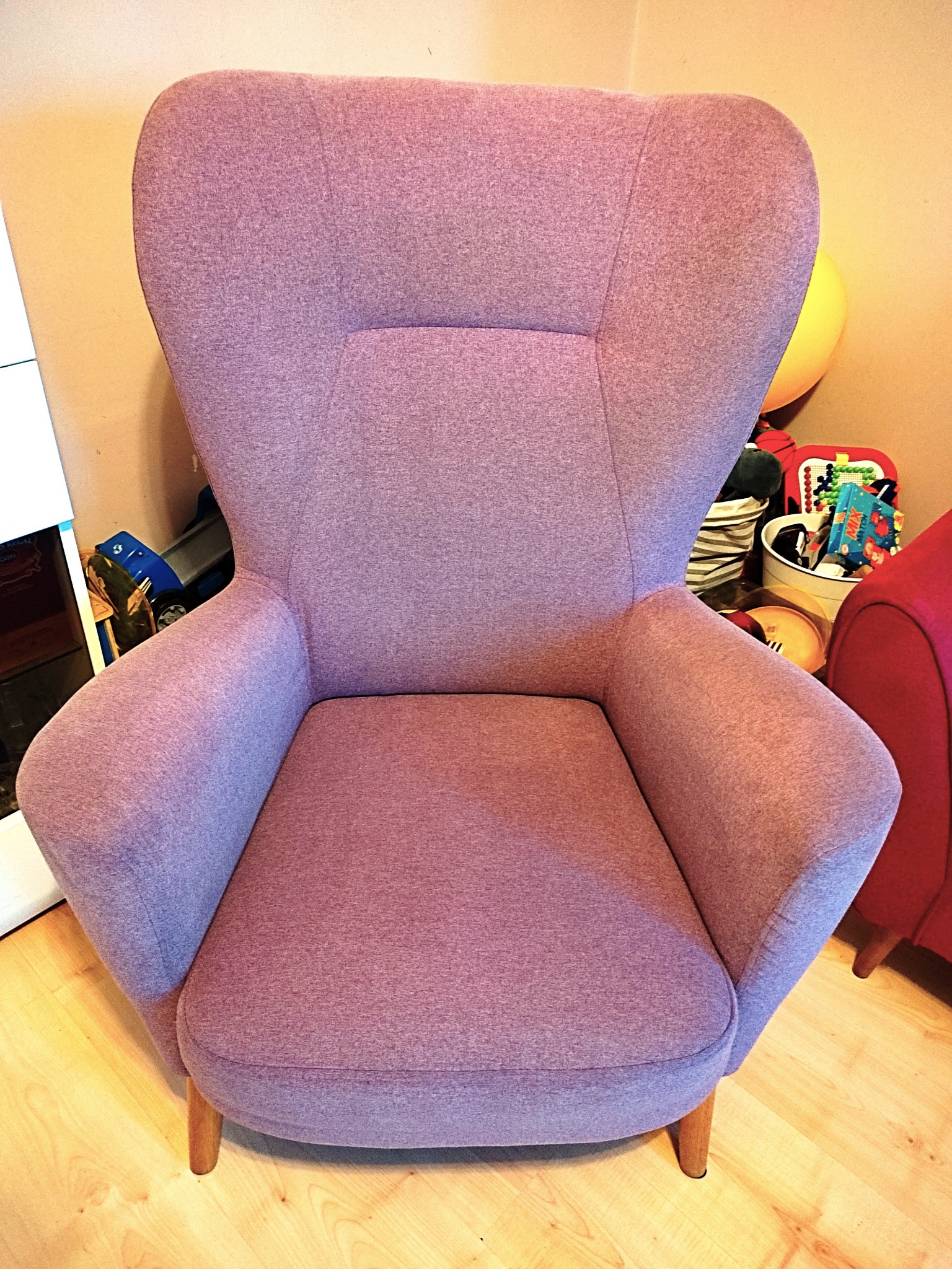 Fioletowy fotel uszak z drewnianymi nóżkami na drewnianej podłodze, z zabawkami i innymi przedmiotami w tle.