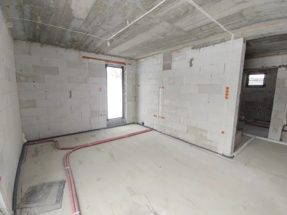 Surowy stan wnętrza z widocznymi przewodami elektrycznymi i rurami grzewczymi, ściany z białego betonu komórkowego, widoczne punkty wyprowadzenia instalacji elektrycznej, przygotowanie do dalszych...