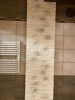 Fragment ściany w łazience wyłożony dekoracyjną, jasną cegłą z widocznymi śladami po fugowaniu, sąsiadujący z brązowymi płytkami i białym grzejnikiem drabinkowym.