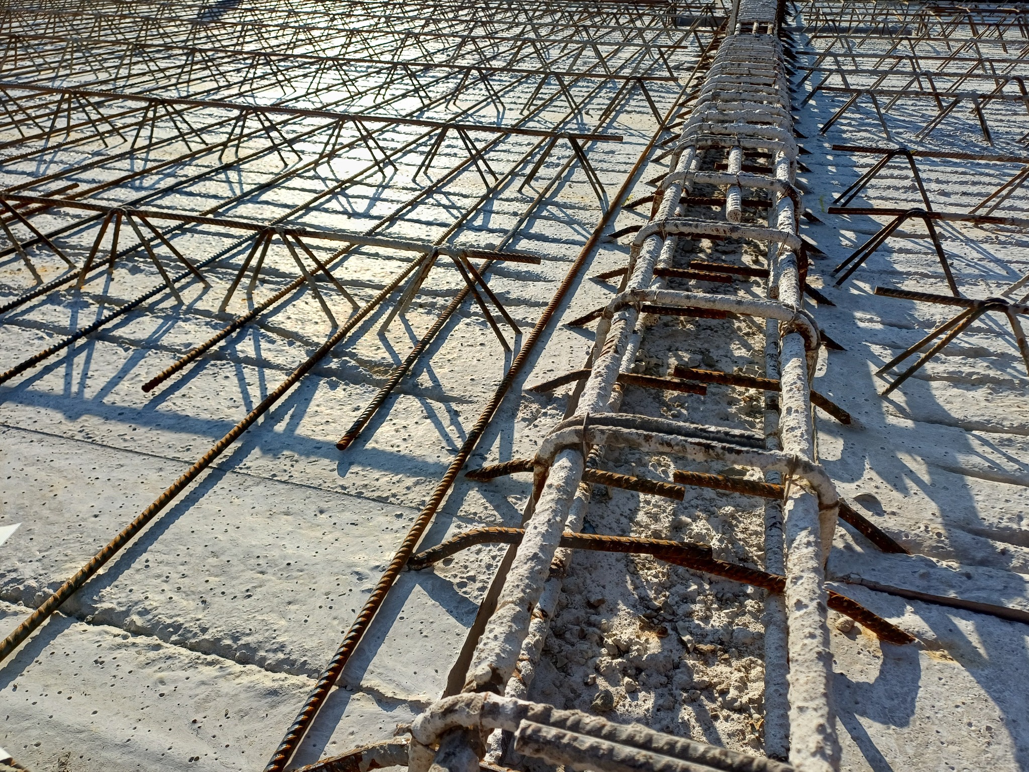 Zbrojenie fundamentu z widoczną siatką stalową i podkładkami dystansowymi. Jasne, kontrastowe oświetlenie podkreśla teksturę betonu i rdzawy odcień stali.
