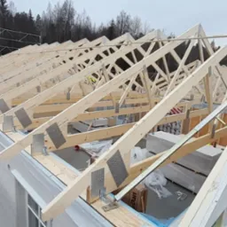 Konstrukcja drewnianego dachu z widocznymi wiązarami kratowymi i metalowymi łącznikami na budowie domu jednorodzinnego, widok z góry.