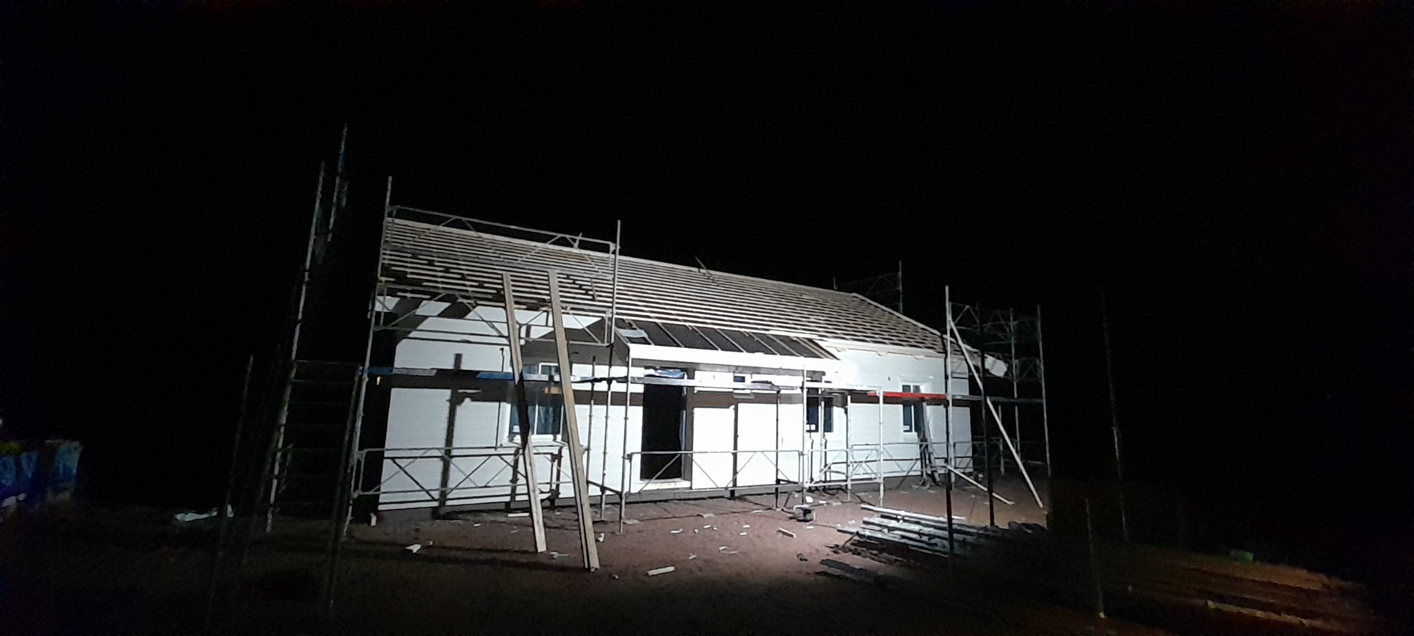 Niedokończony budynek jednorodzinny w nocy, otoczony rusztowaniem, z widoczną konstrukcją dachu.