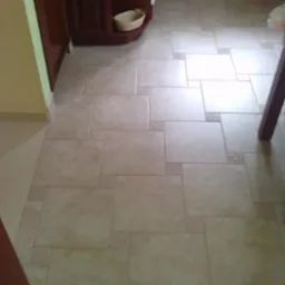 Beżowa podłoga z płytek ceramicznych ułożonych w geometryczny wzór w kuchni. Dekoracyjne, kwadratowe płytki oddzielają większe prostokątne.