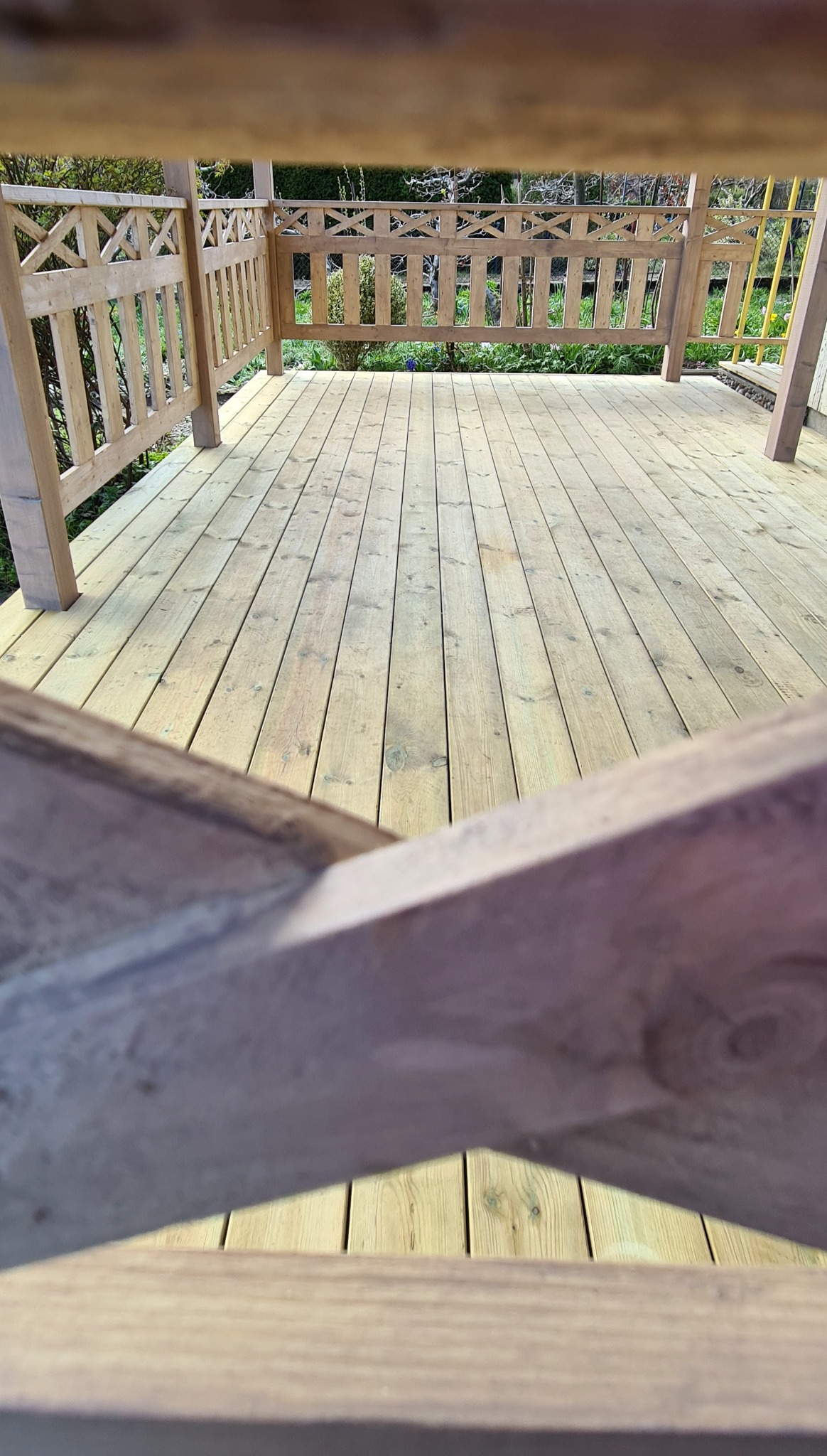 Nowy, jasny drewniany podest z ozdobnymi balustradami w altanie, widok z dołu na deski i konstrukcję.