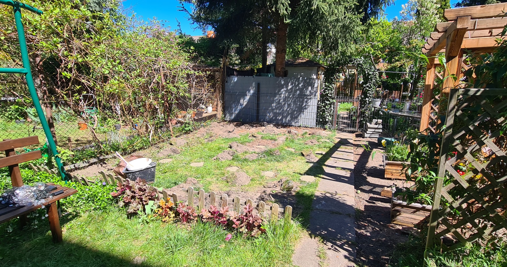 Przygotowany teren pod budowę tarasu drewnianego w ogrodzie. Widoczne wykopane dołki, częściowo ogrodzony teren i elementy konstrukcyjne pergoli.