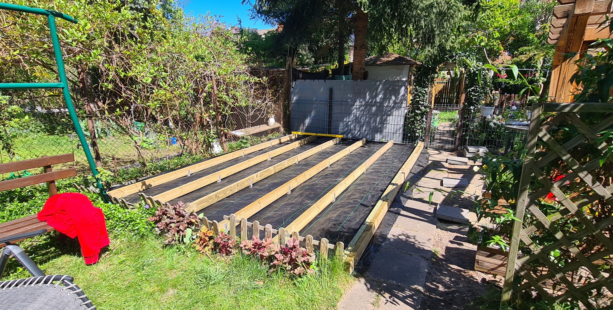 Konstrukcja pod taras drewniany w Redzie: drewniane legary na czarnej macie, ogrodzenie z palików, zieleń w tle. Etap budowy tarasu.