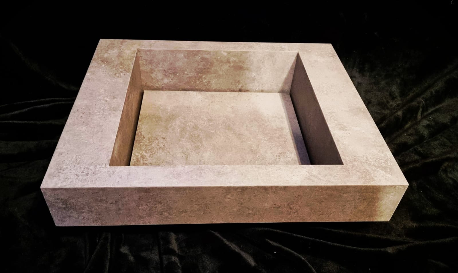 Kwadratowa umywalka z beżowych płytek imitujących kamień, nowoczesny design na ciemnym tle.