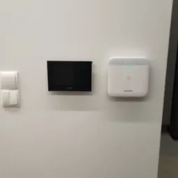 Panel sterowania Dahua i centrala alarmowa Hikvision zamontowane na białej ścianie, obok włącznika światła.