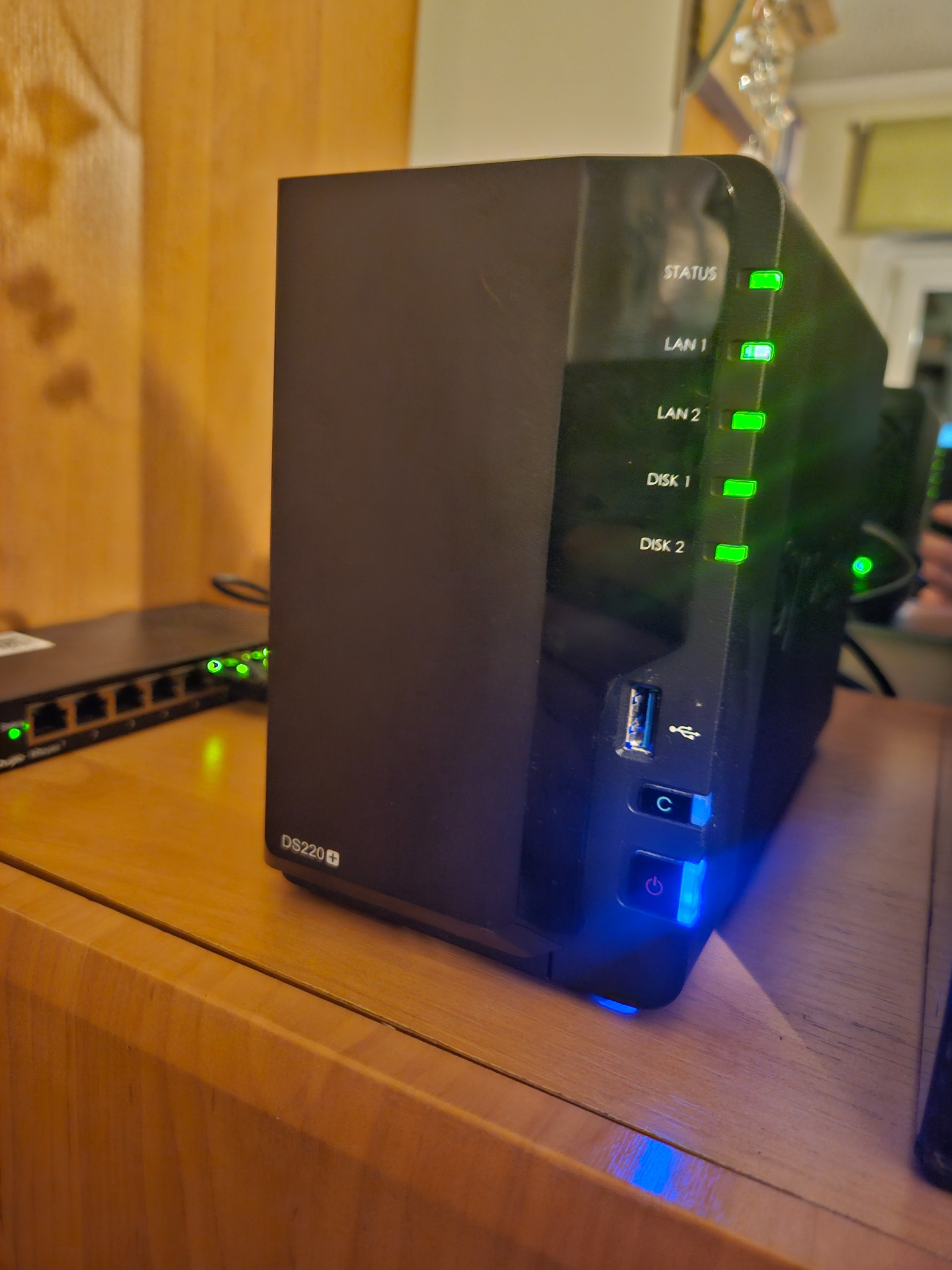 Konfiguracja serwera NAS Synology DS220+ z aktywnymi diodami LED, widoczny router sieciowy w tle, Lubań.