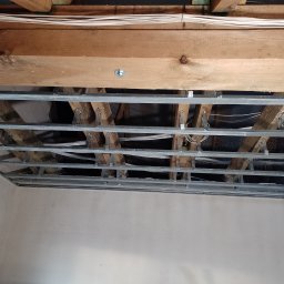 Radosław Butryński Korso-Remonty - Konstrukcja metalowa podwieszanego sufitu zamontowana do drewnianych belek stropowych, widoczne przewody elektryczne, ściany przygotowane pod malowanie we Wrocławiu.