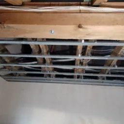 Konstrukcja metalowa podwieszanego sufitu zamontowana do drewnianych belek stropowych, widoczne przewody elektryczne, ściany przygotowane pod malowanie we Wrocławiu.