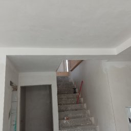 Radosław Butryński Korso-Remonty - Wnętrze w trakcie prac wykończeniowych: surowe schody betonowe, ściany po nałożeniu gładzi, widoczny poziomica, otwór drzwiowy z widocznymi bloczkami i zapiskami, sufit z gładzią