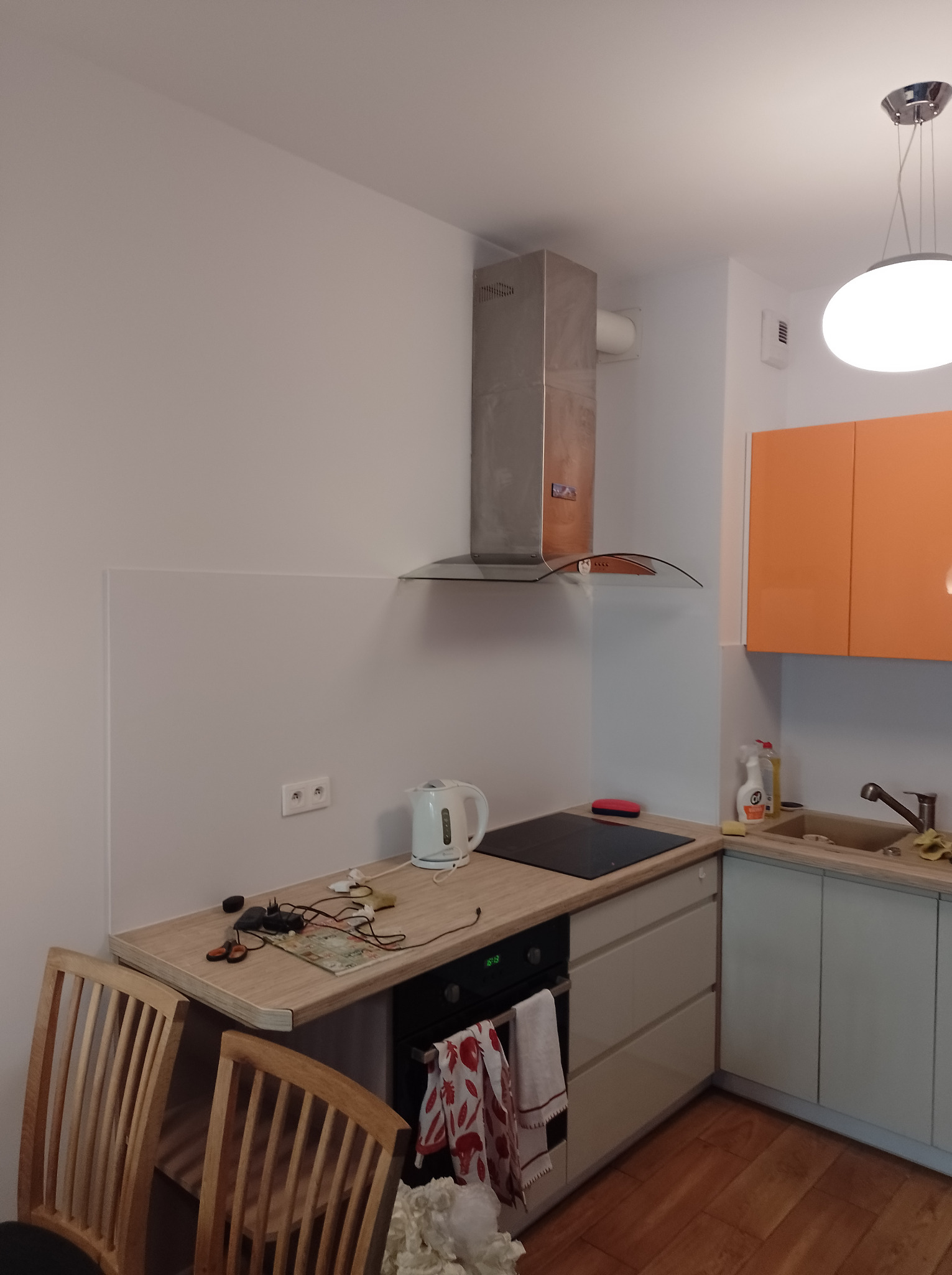 Wnętrze kuchni we Wrocławiu przed drobnymi poprawkami: widoczne białe ściany, jasne blaty, pomarańczowe szafki, srebrny okap i drobne przedmioty na blacie.