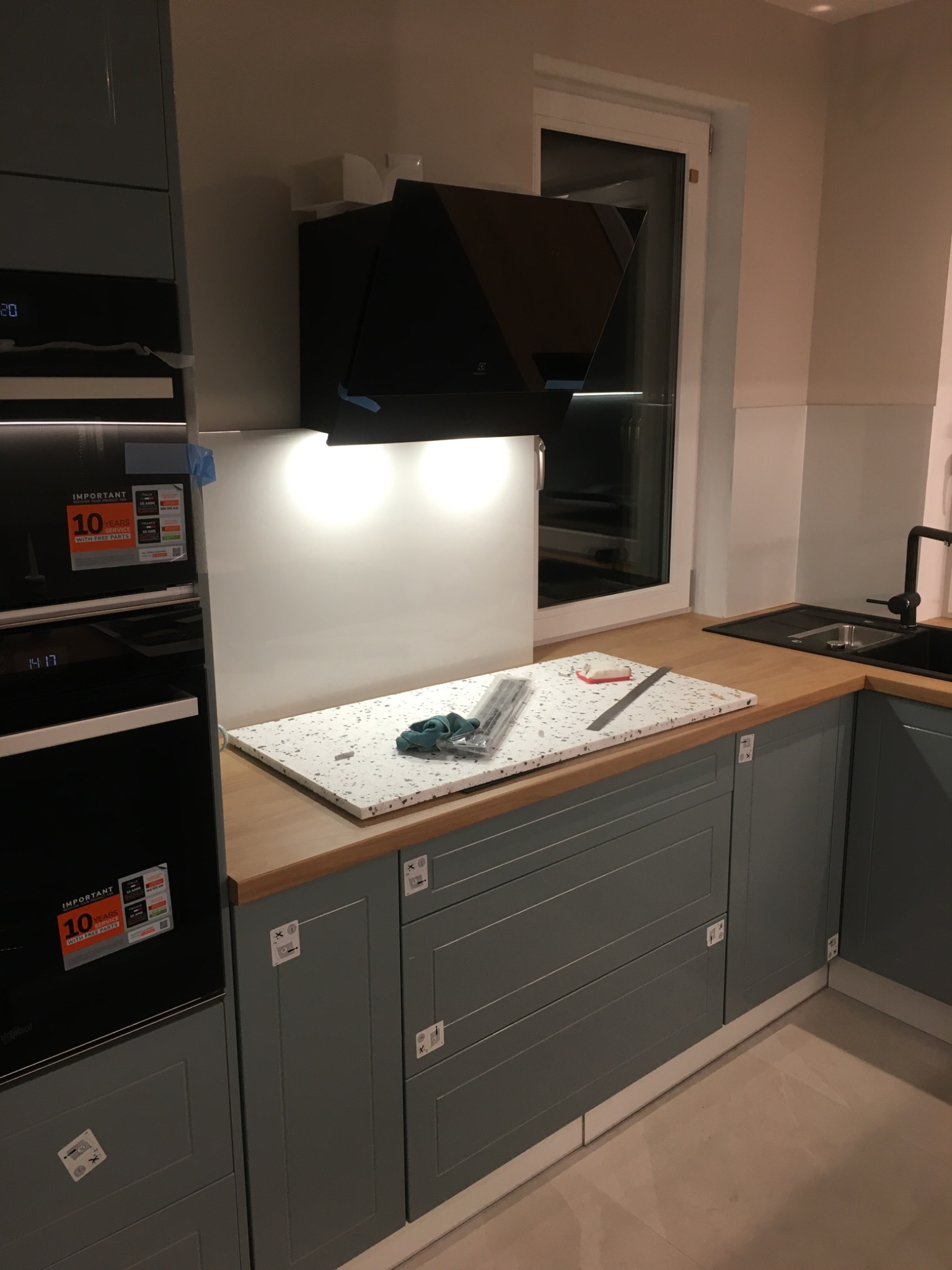 Wnętrze kuchni w Kościerzynie w trakcie montażu blatu z lastryko, widoczny okap, zlew i płyta grzewcza z naklejonymi foliami ochronnymi.