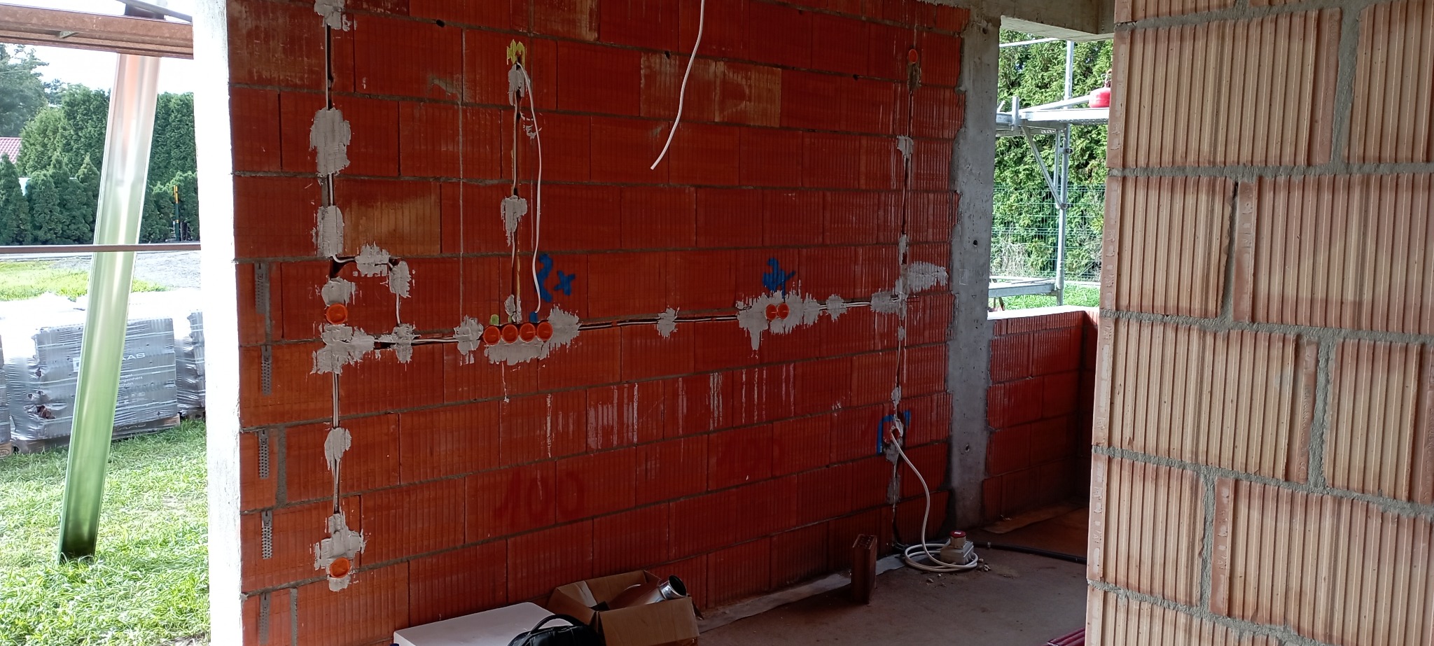 Instalacja elektryczna w trakcie montażu w surowym budynku z czerwonej cegły, widoczne kable, puszki elektryczne i zaprawa murarska.