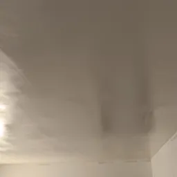 Świeżo nałożona, mokra warstwa na suficie, odbijająca światło, widoczne nierówności i smugi, przygotowana do dalszej obróbki.