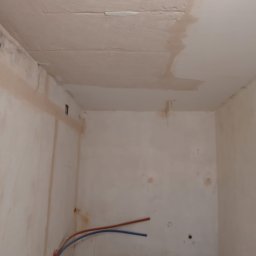 Adam Rączka - Pokój po szpachlowaniu, widoczne ślady na ścianach i suficie, rury instalacji wodnej przy podłodze. Przygotowanie do dalszych prac wykończeniowych.