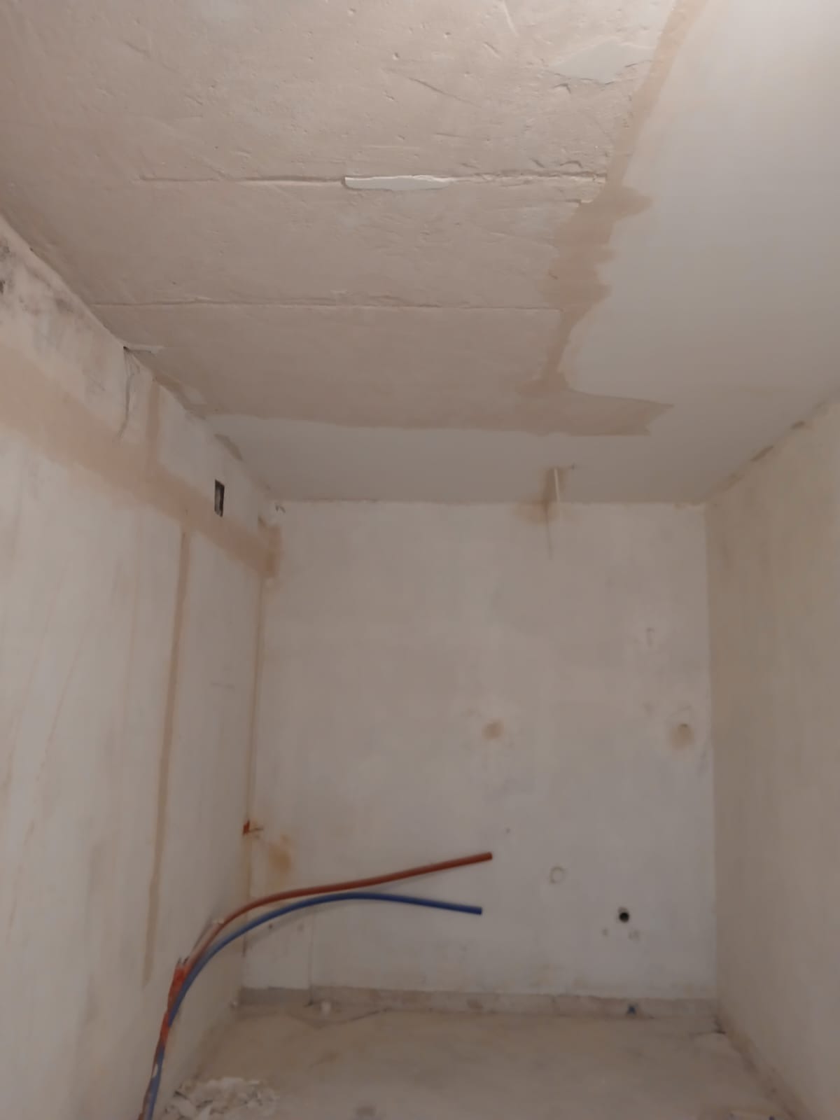 Pokój po szpachlowaniu, widoczne ślady na ścianach i suficie, rury instalacji wodnej przy podłodze. Przygotowanie do dalszych prac wykończeniowych.