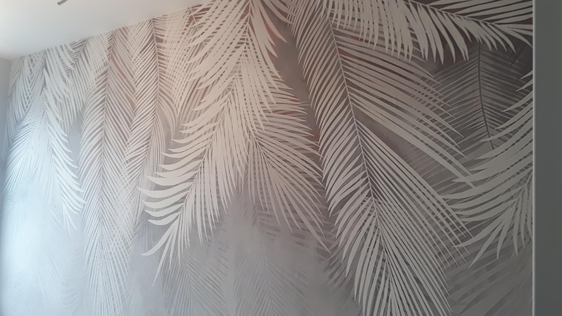 Ściana w sypialni pokryta fototapetą z motywem białych liści palmowych na szarym tle.