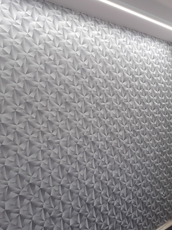 Ściana pokryta tapetą z geometrycznym wzorem trójkątów w odcieniach szarości, oświetlona listwą LED przy suficie.